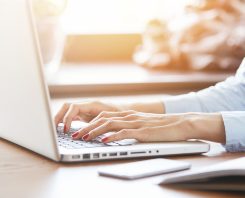 Cropped shot of woman's hands with red nails typing on keyboard